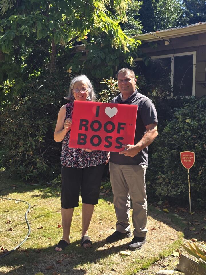 Two people holding an I love ROOF BOSS sign outside a home